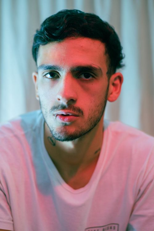 Free Close-up portrait of a young man with black hair and stubble wearing a white t-shirt indoors. Stock Photo
