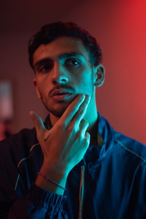 Free Close-up portrait of a young man with thoughtful expression under neon lighting, highlighting facial features and mood. Stock Photo
