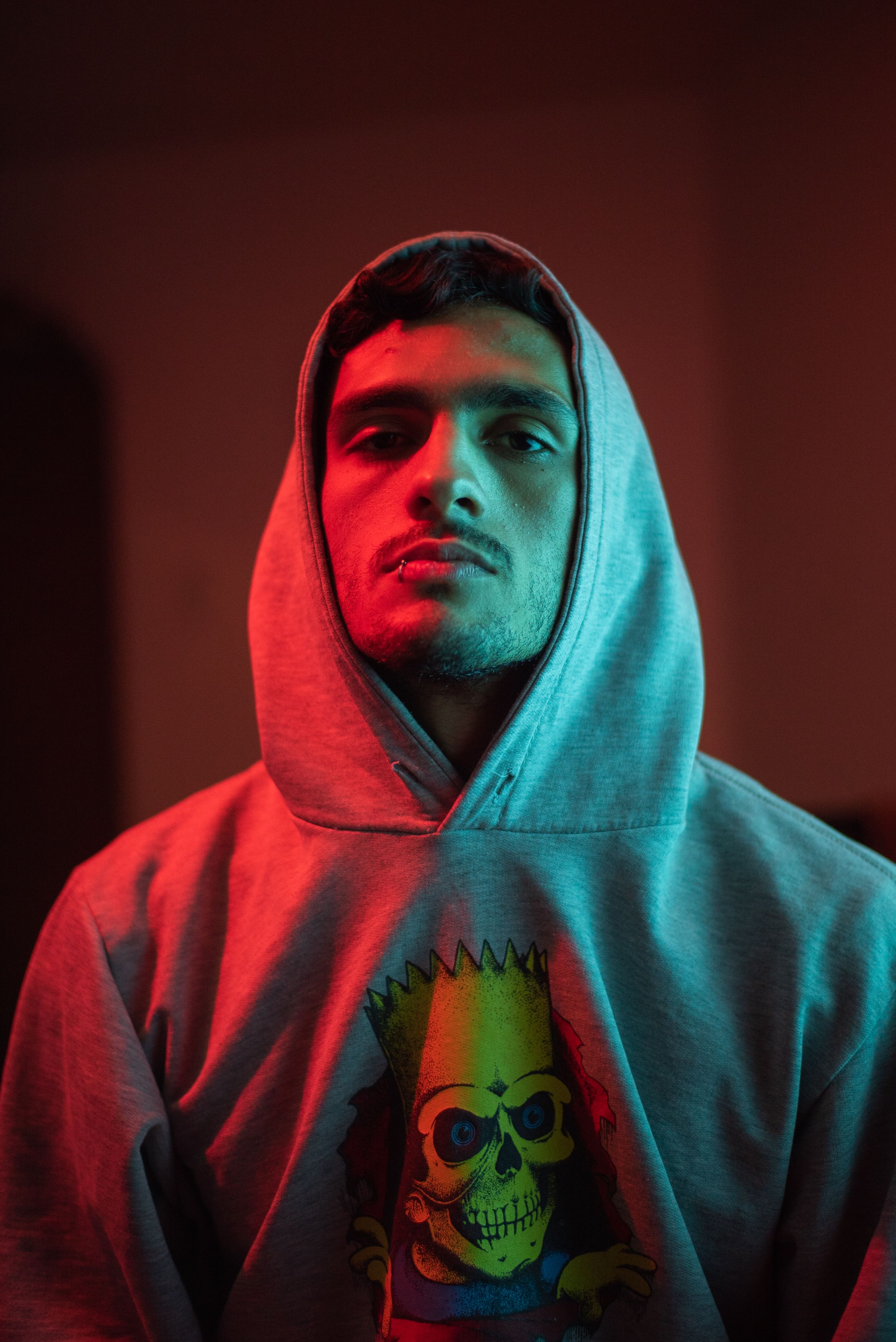 Portrait of a man in a hoodie under neon light, creating a dramatic, moody atmosphere.