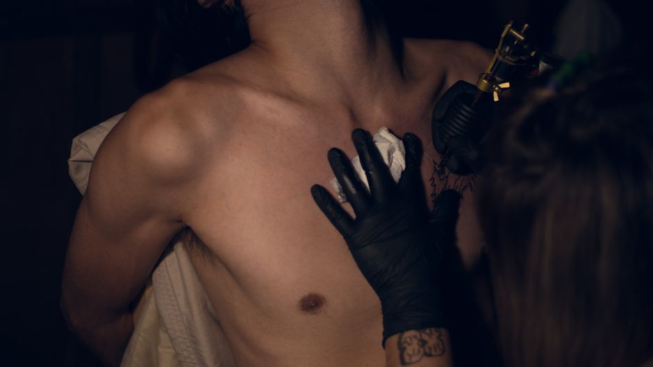 An artist tattoos a man's chest in a dimly lit tattoo shop setting. An artist tattoos a man's chest in a dimly lit tattoo shop setting.