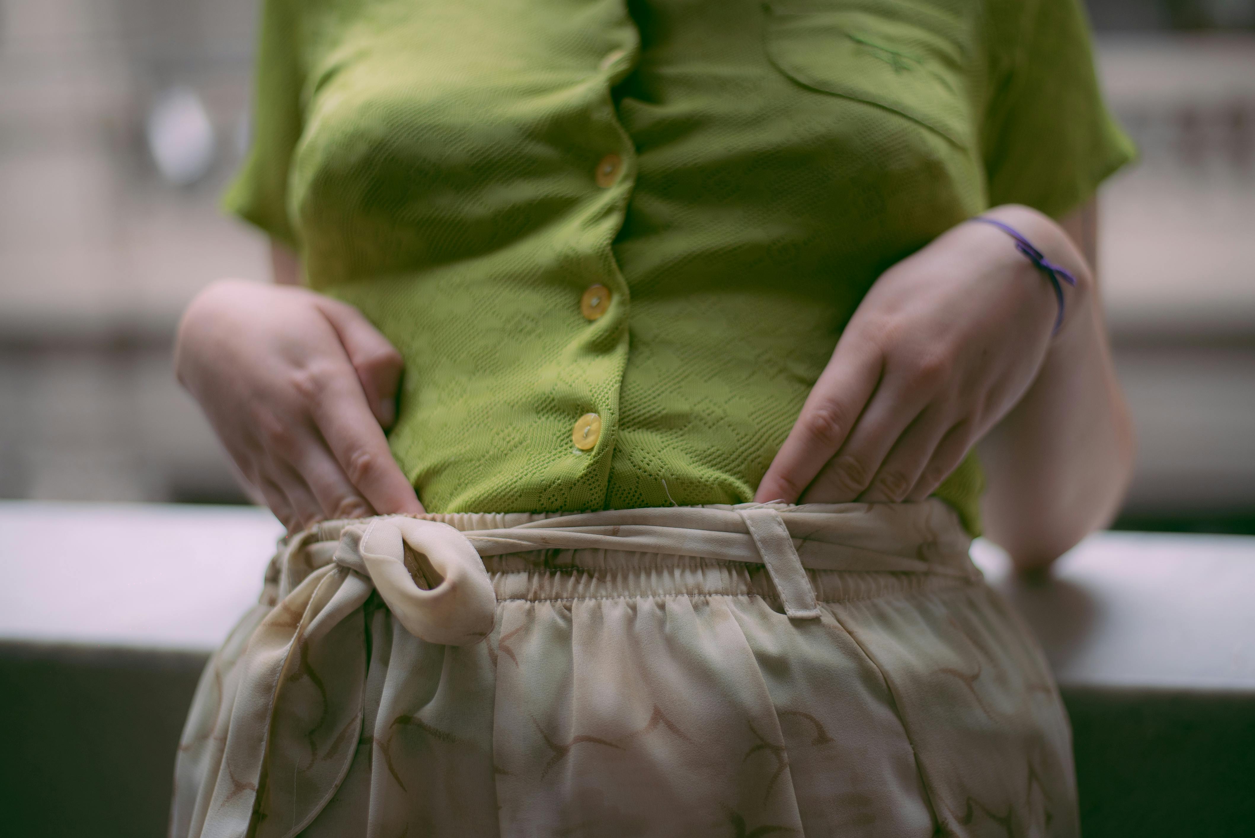 Close-up of a woman wearing a stylish green blouse and beige skirt outdoors.