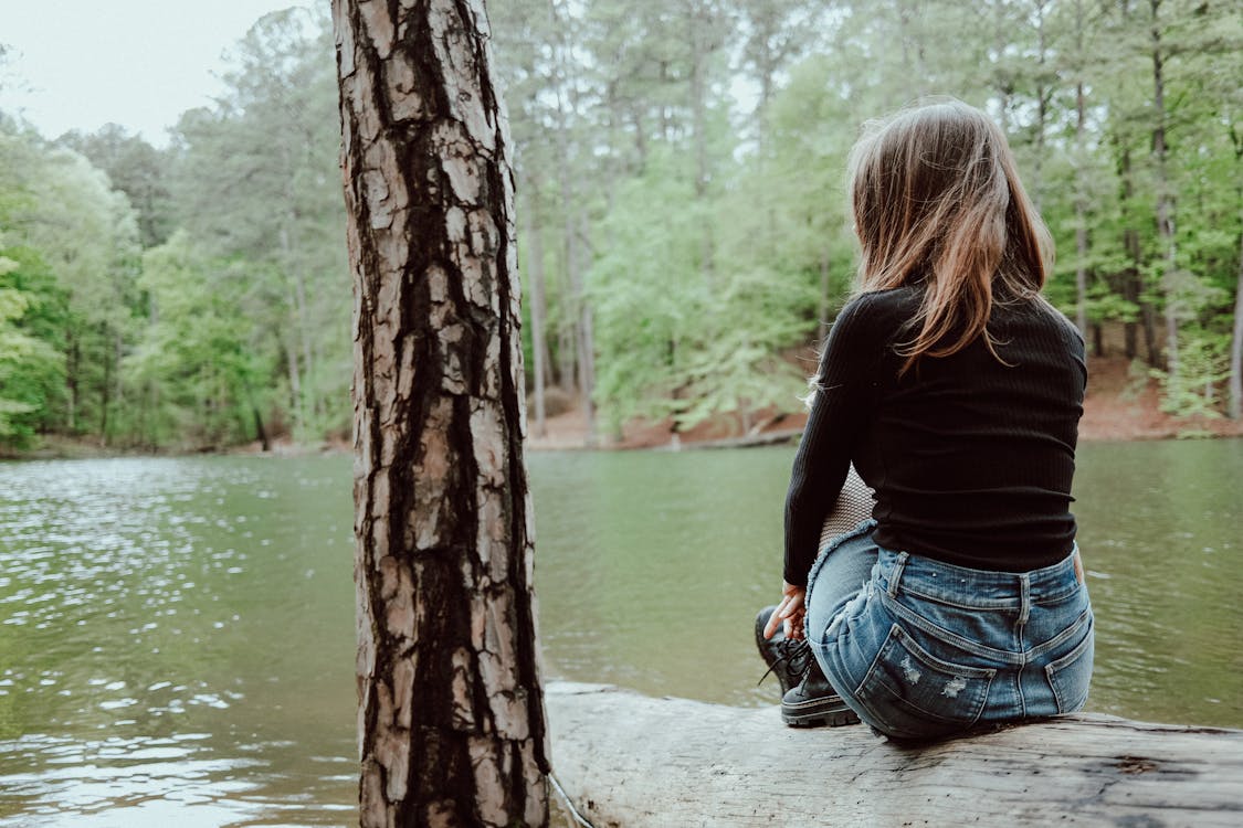 A girl sitting on a log in front of a lake