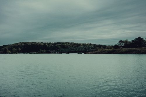 Free A tranquil scene featuring a bridge over water under a cloudy sky, surrounded by lush greenery. Stock Photo