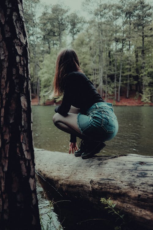 A woman crouching on a log in front of a lake