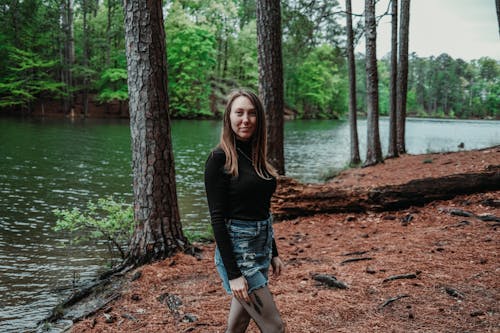 A girl standing in front of a lake in the woods