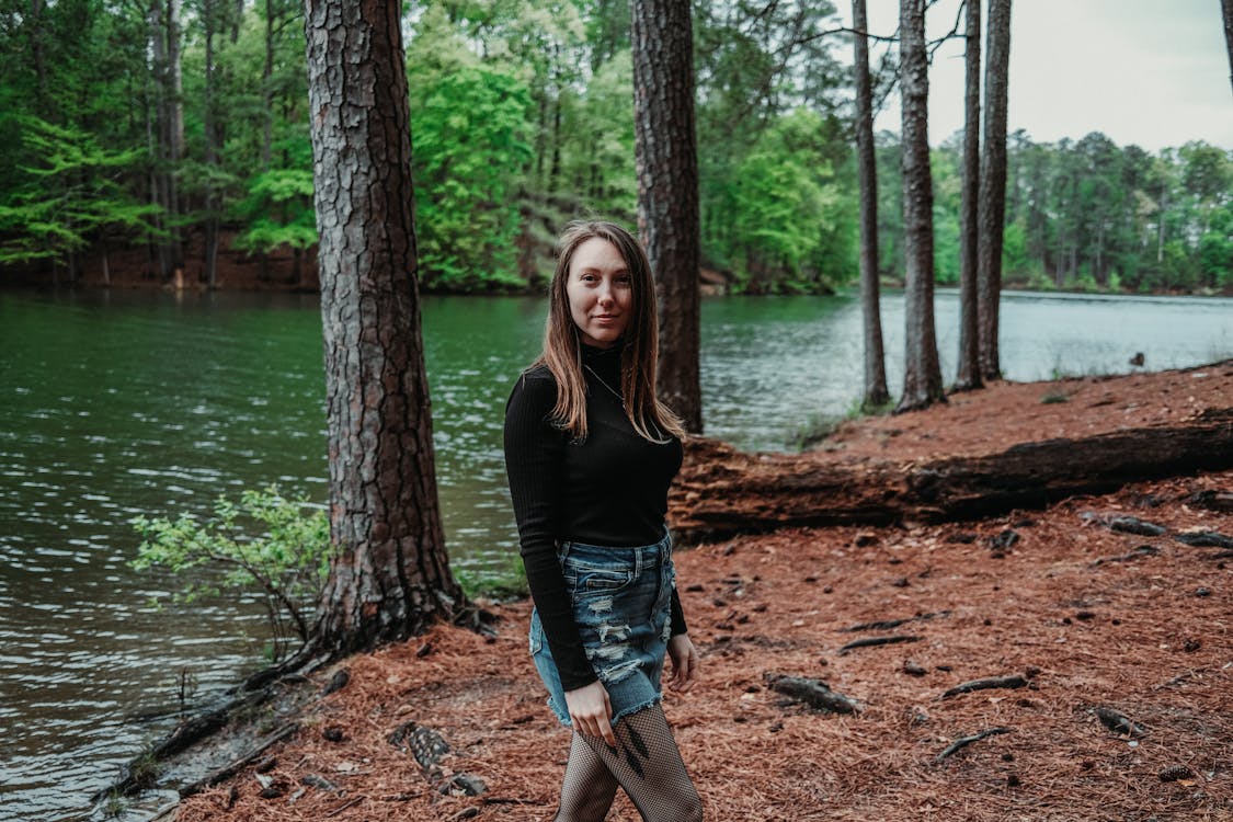 A girl standing in front of a lake in the woods
