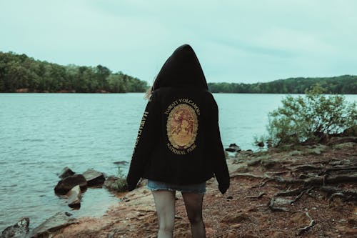 A woman standing on the shore of a lake wearing a hoodie with a patch on it