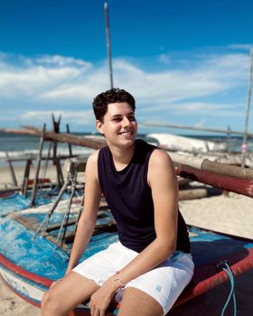 Man smiling on a beach beside a moored boat, enjoying a sunny summer day.