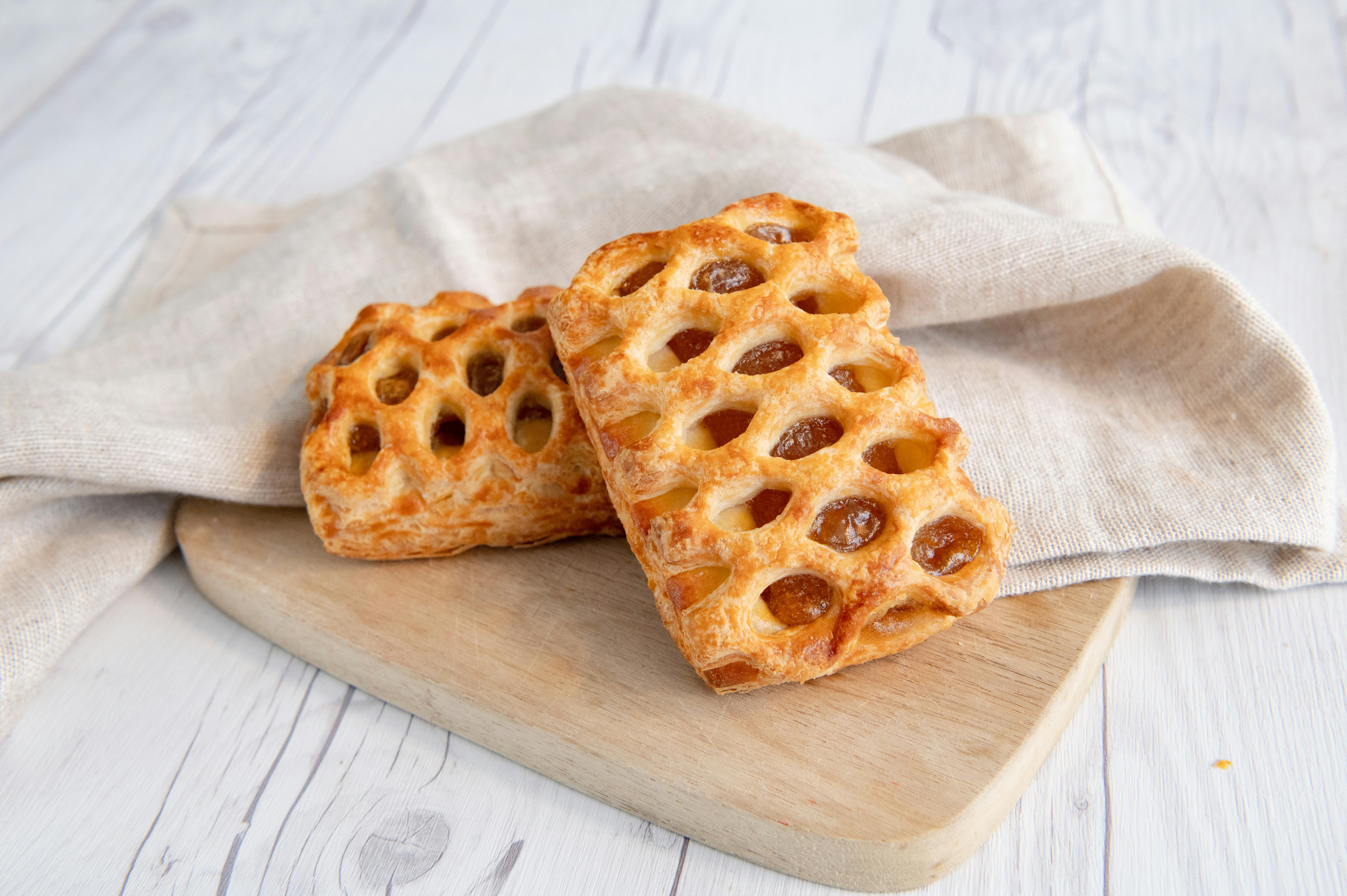 Close-up of two freshly baked danish pastries with a lattice pattern on a wooden board.