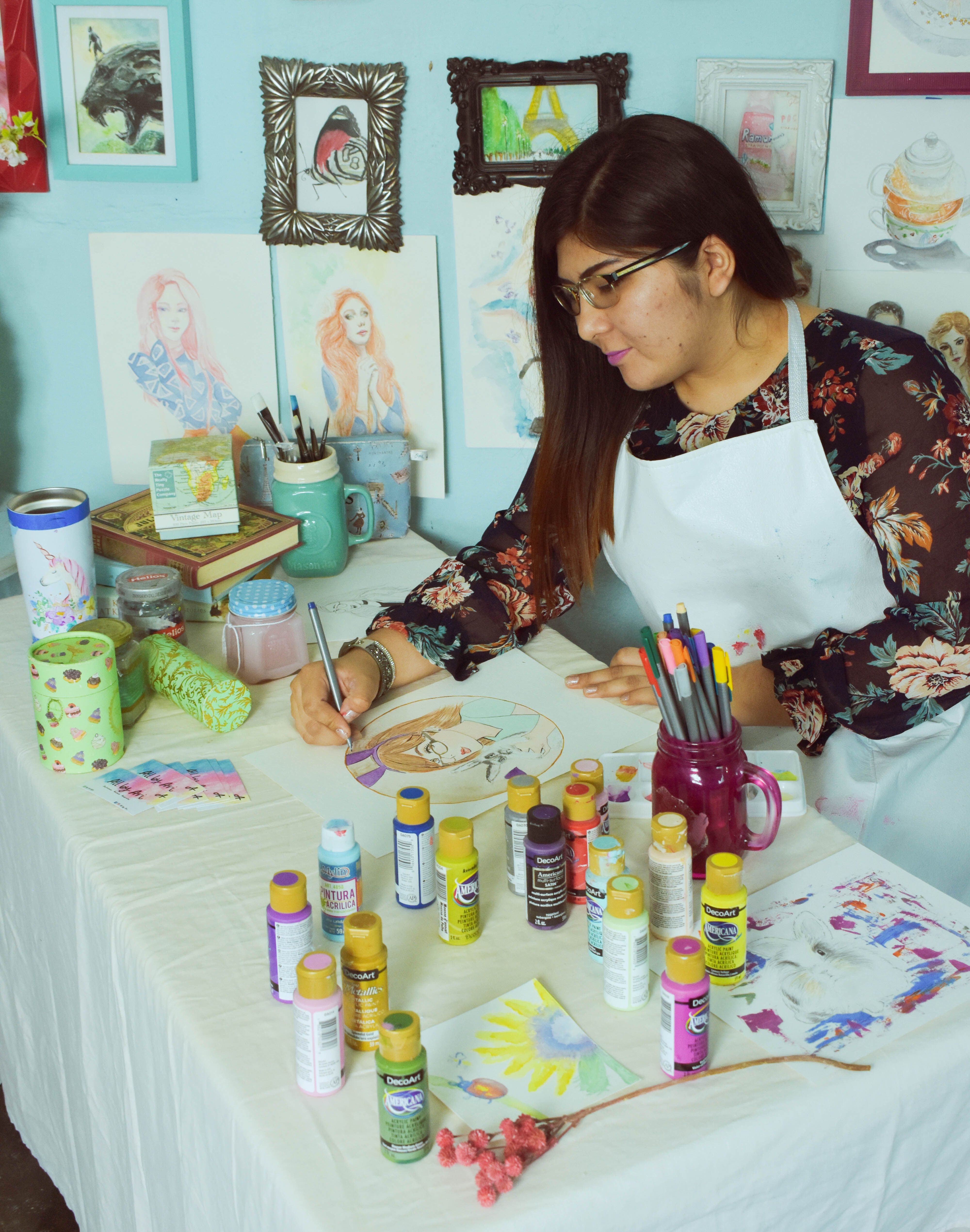 Female artist paints a portrait in a vibrant, creative workspace filled with art supplies.