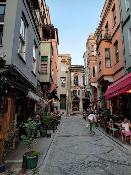 Free Explore a narrow cobblestone street lined with vibrant buildings and outdoor cafes, capturing urban life. Stock Photo