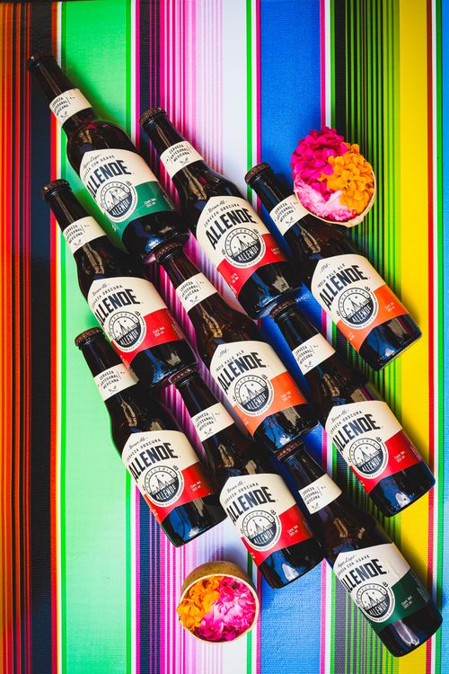 Free Patterned arrangement of Allende beer bottles on vibrant Mexican textile with flowers. Stock Photo