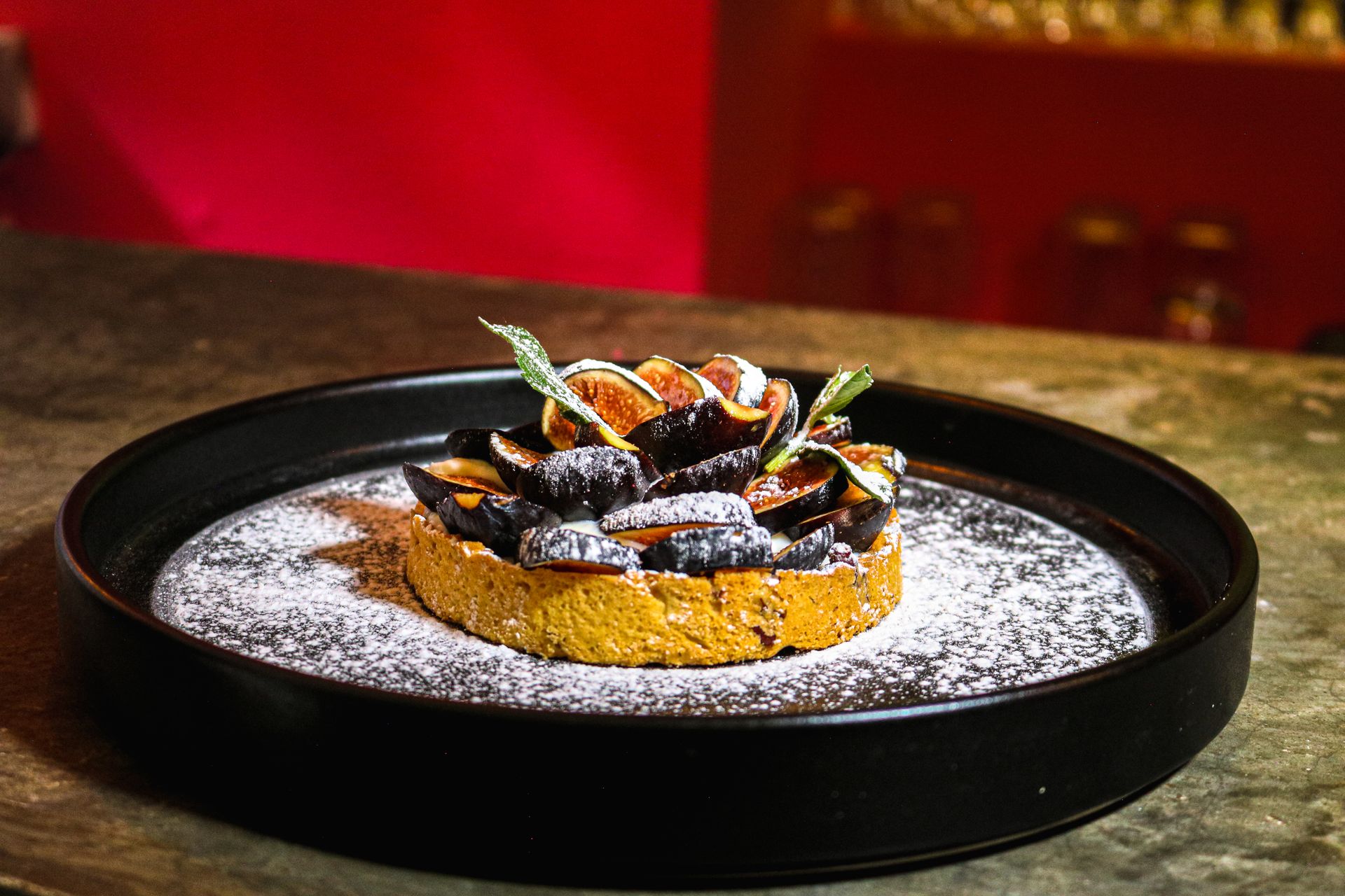 Close-up of a sumptuous fig tart in Ciudad de México, beautifully dusted with sugar on a dark plate.