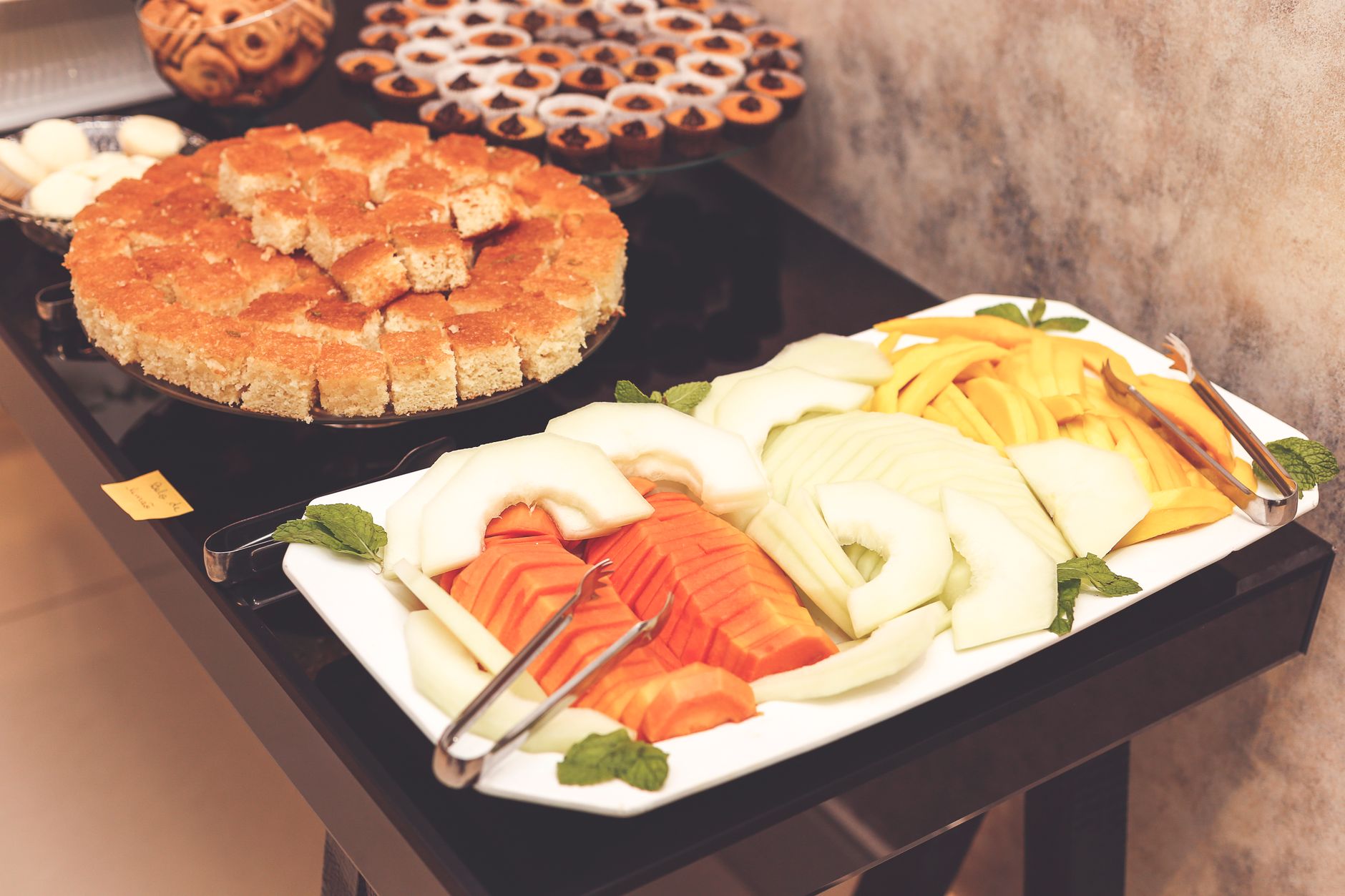 A vibrant and delicious buffet with cut fruit and desserts ready to serve.
