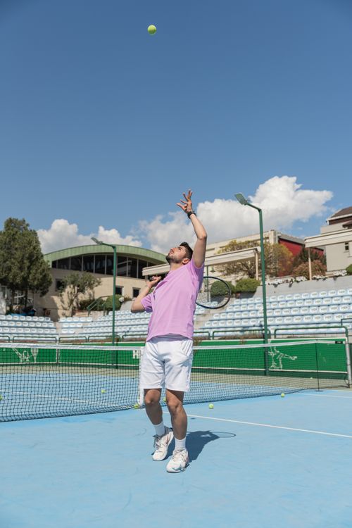 Free Adult male tennis player in action, serving on a sunny outdoor court with blue sky. Stock Photo