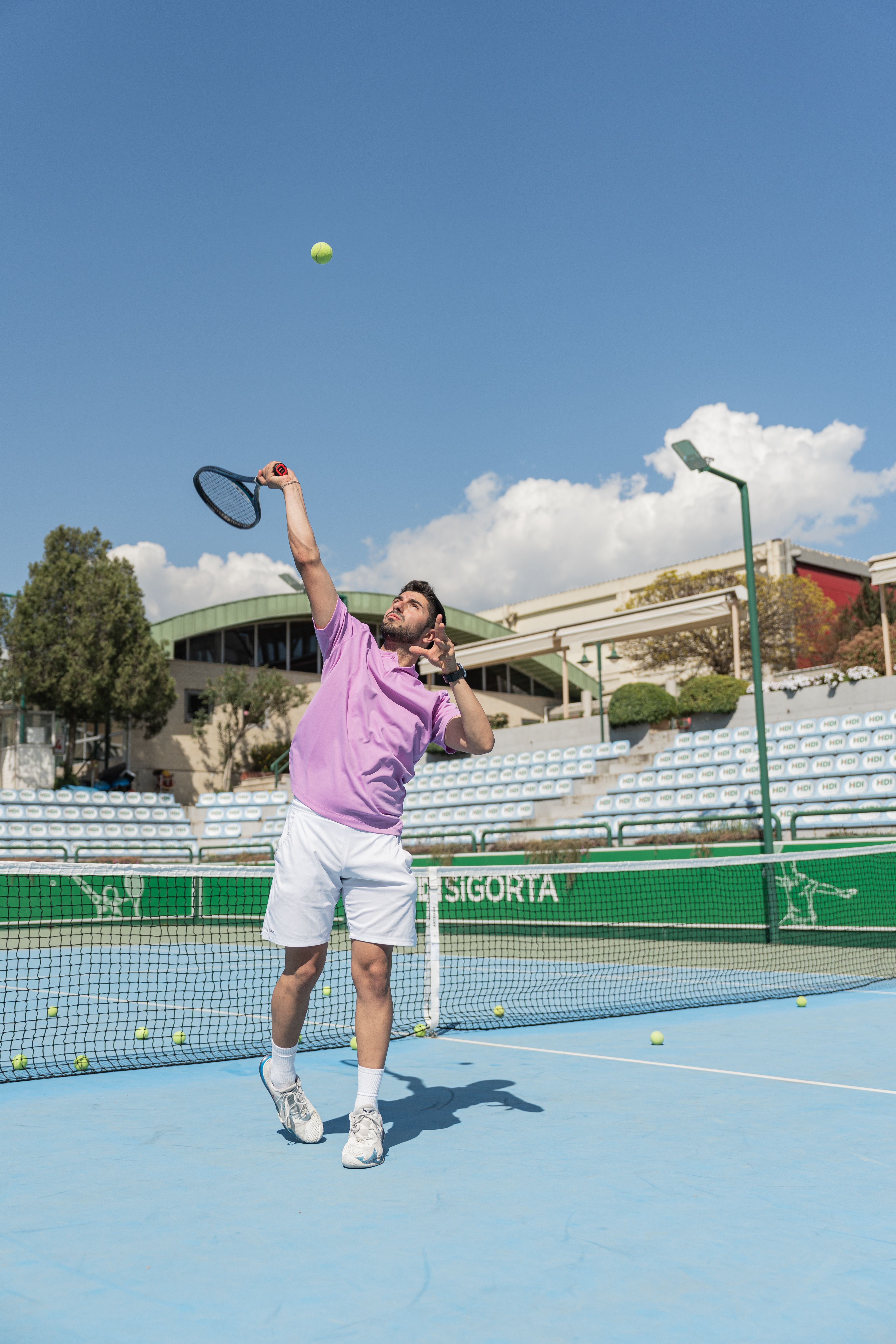 A tennis player in motion serving on an outdoor court under a clear blue sky.