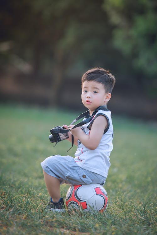 Boy Sitting On Soccer Ball Holding Dslr Camera