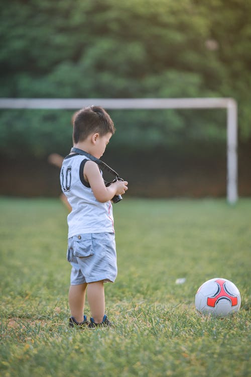 Boy Standing Using Dslr Camera Near Soccer Ball