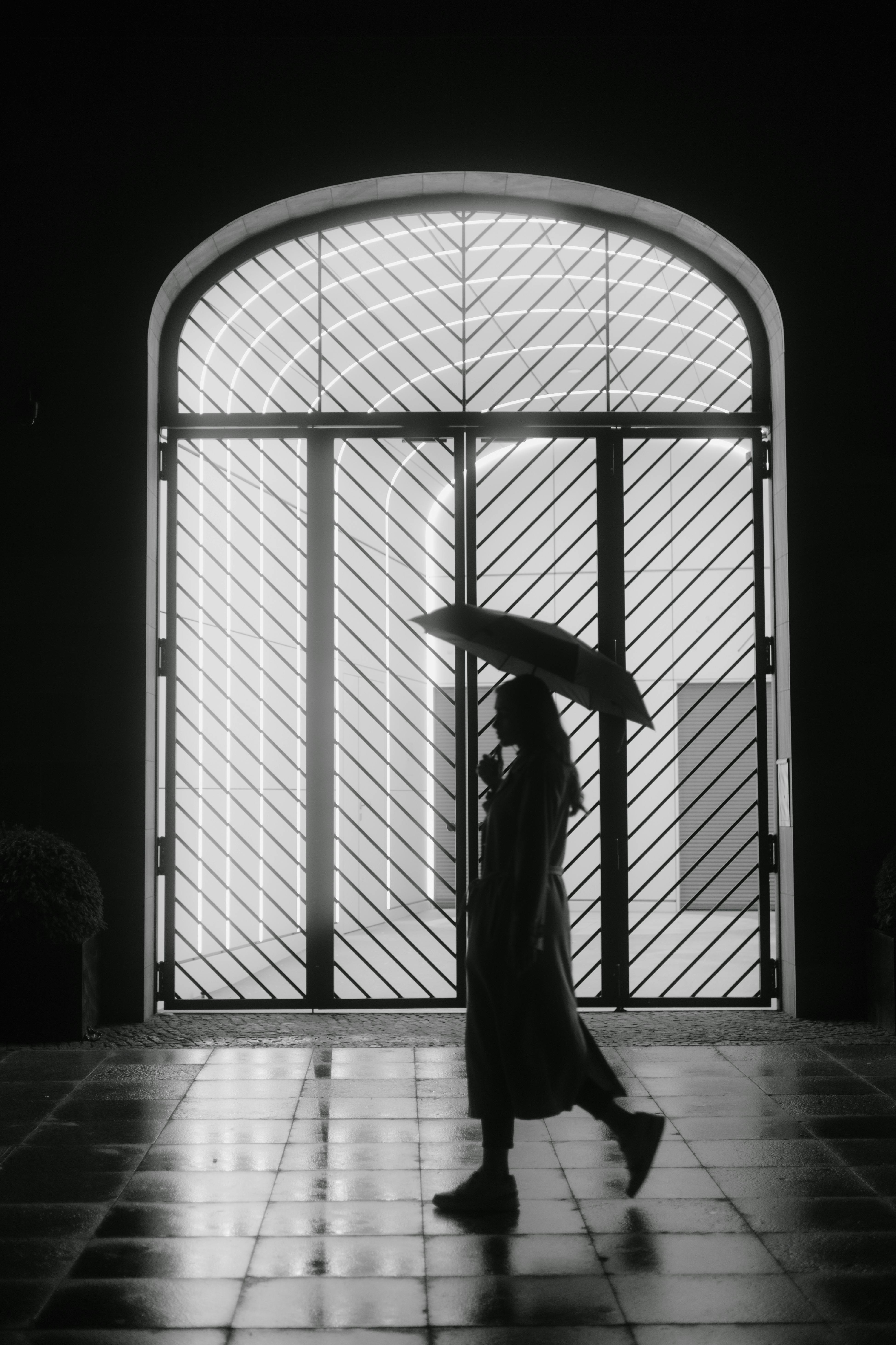 Silhouette of a woman holding an umbrella walking past a decorative window in Berlin.