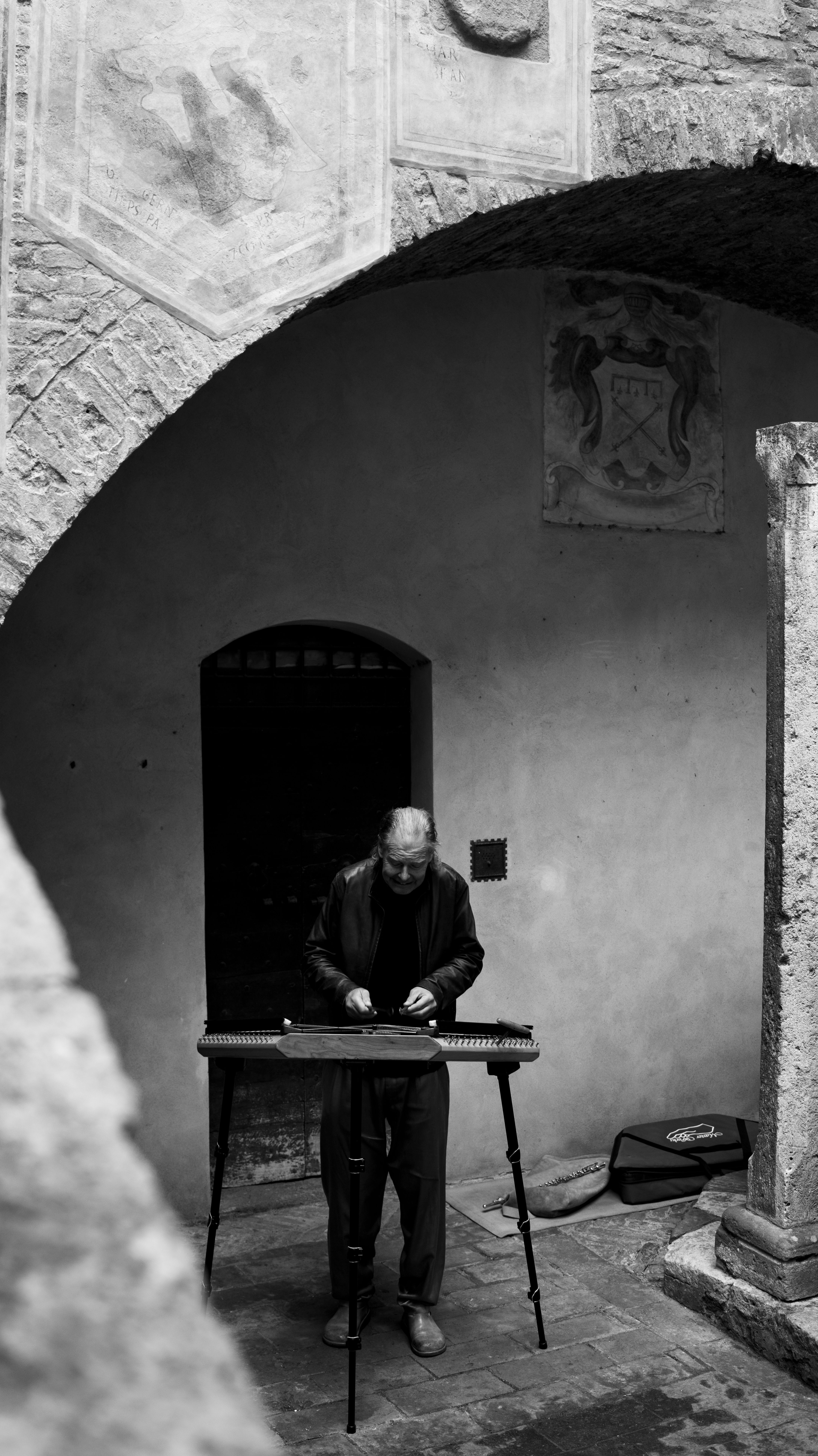 A street musician plays a unique instrument under an arched structure, creating a historic ambiance.