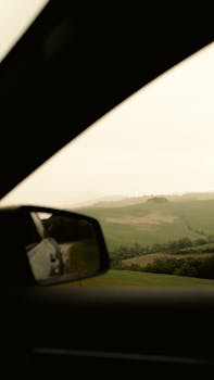 Peaceful countryside landscape viewed from inside a car with rolling green hills.