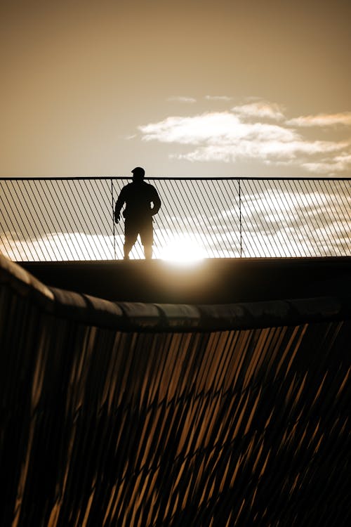 A man is standing on a bridge at sunset