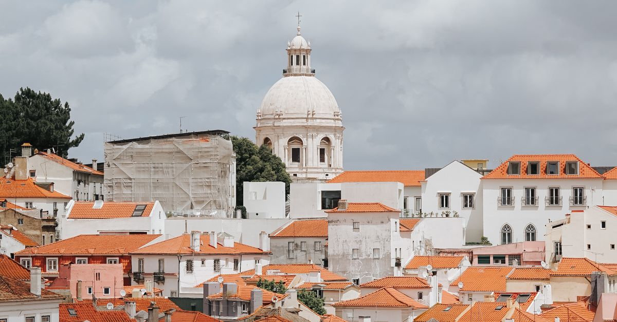 Panoramic view of Lisbon's iconic terracotta rooftops and historic architecture under a cloudy sky.