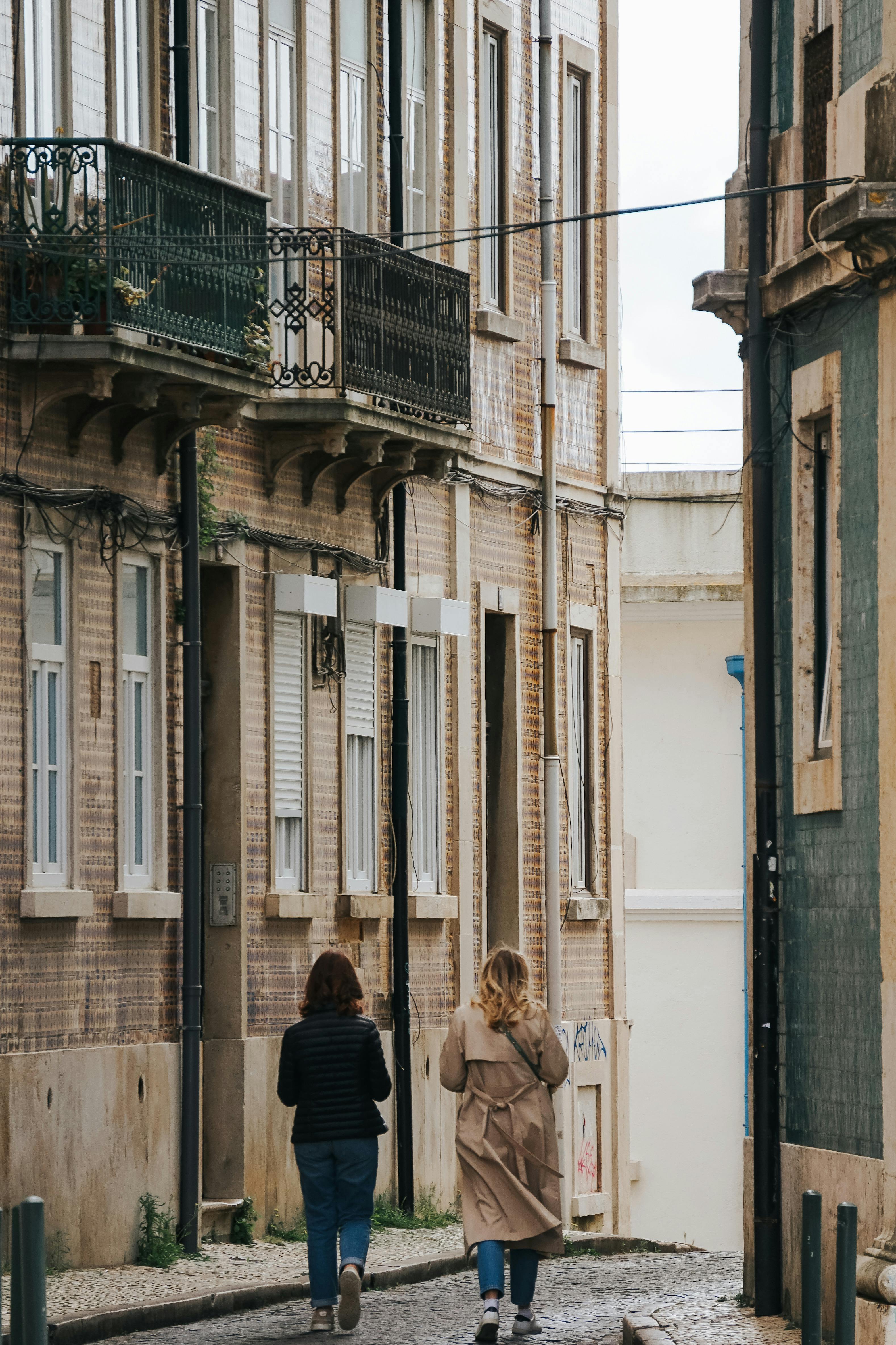 Two women walking along a narrow European street, surrounded by vintage architecture.