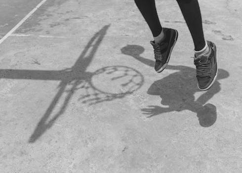 Black and white photo capturing a jump on an outdoor basketball court with shoe shadows.