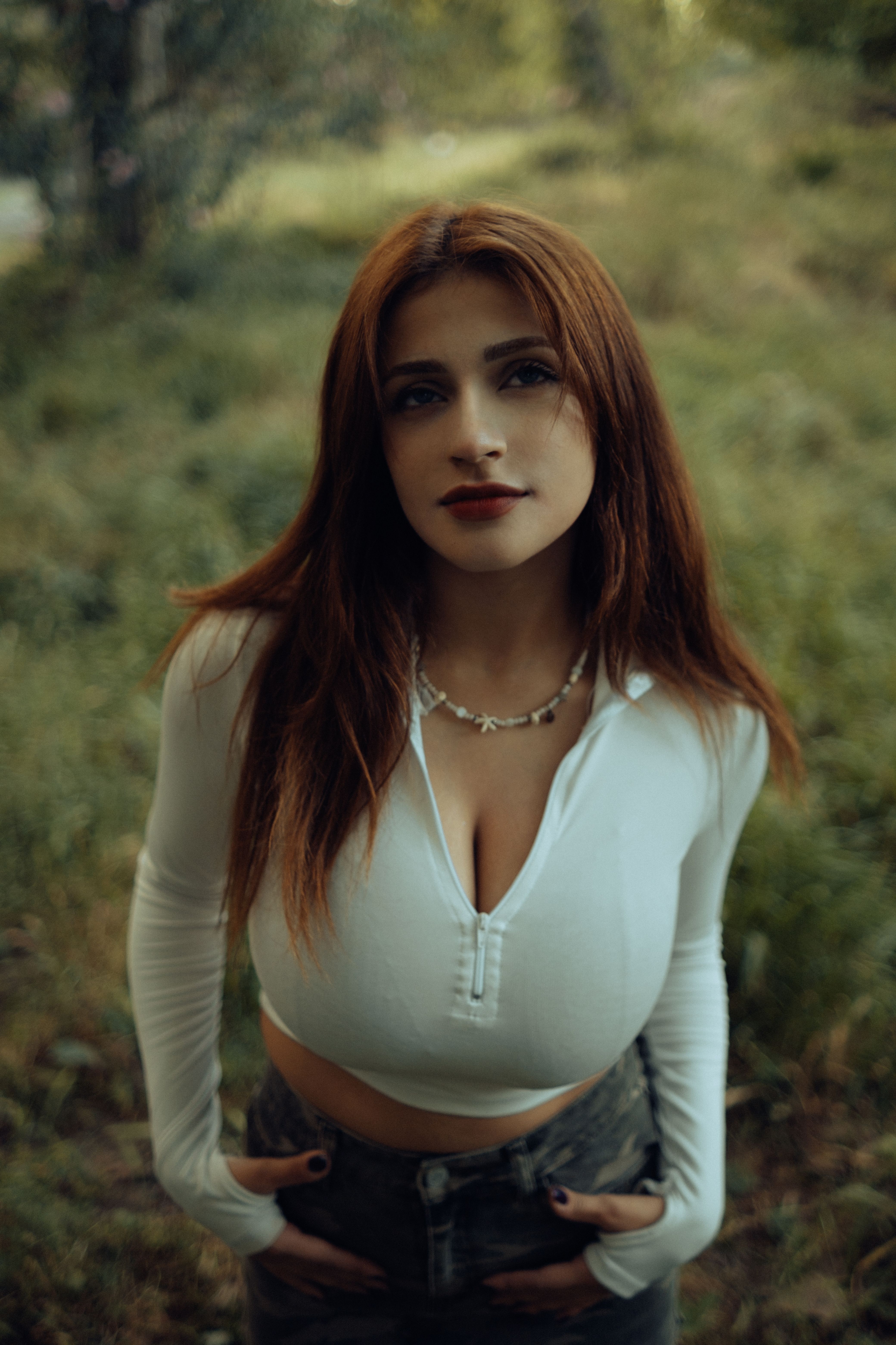 Red-haired woman in a crop top smiling outdoors in a park setting.