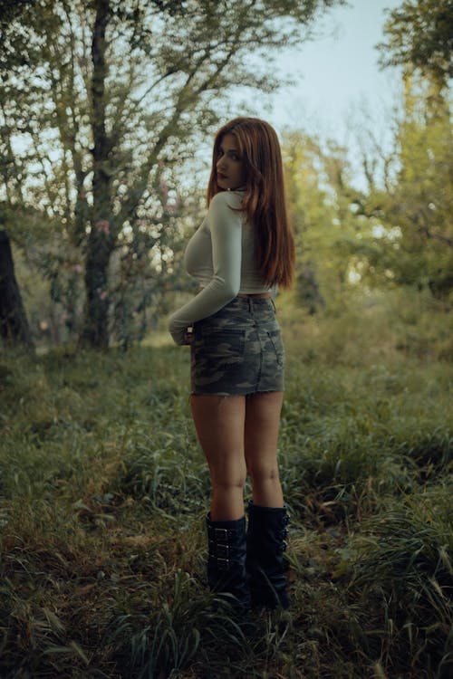 A woman in a skirt and boots standing in the woods