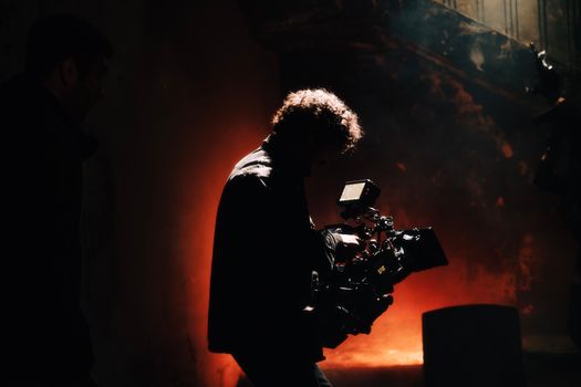A professional cameraman captures footage in a creatively lit, moody setting, backlit by warm light.