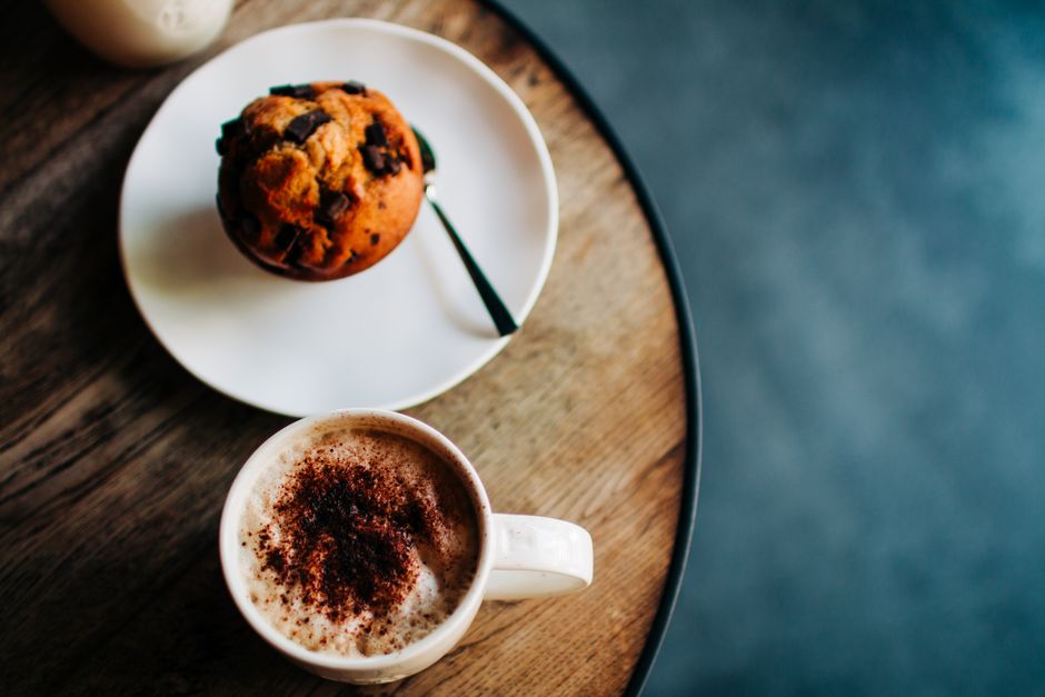 A top view of a chocolate muffin and coffee on a rustic table, creating a cozy café vibe.