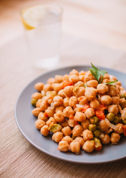 A plate of chickpeas with vegetables and a glass of water