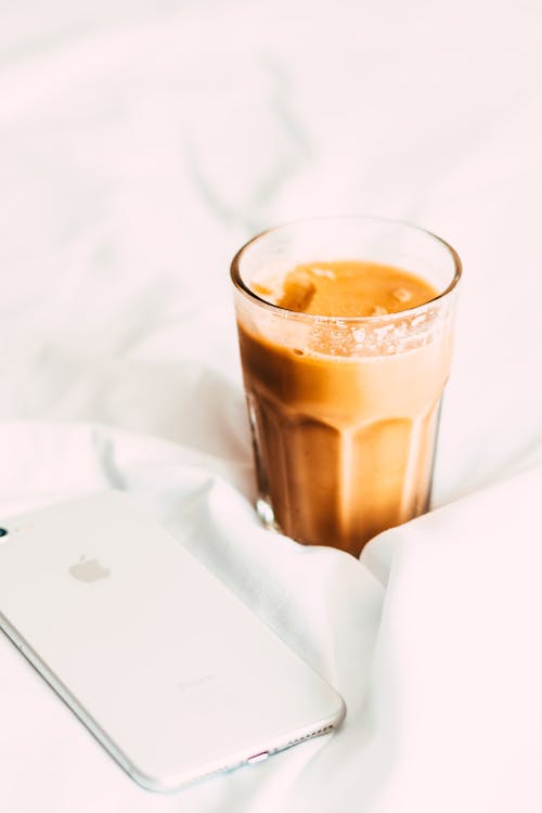 A glass of coffee and an iphone on a bed