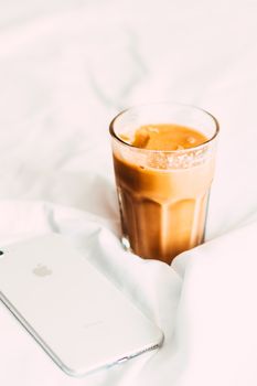 A refreshing iced coffee next to a smartphone on white fabric, perfect for a relaxed morning vibe.