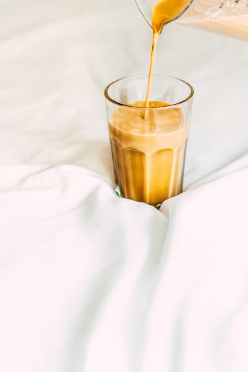 A person pouring coffee into a glass on a bed