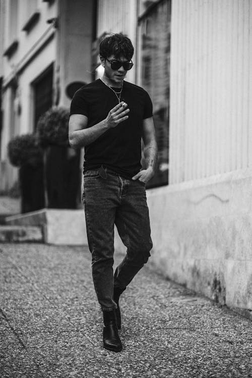 A man in black shirt and jeans walking down the street