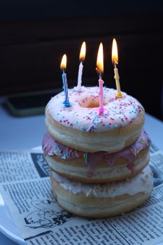 Stacked donuts with lit candles on newspaper create a unique birthday idea.