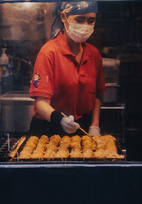Free Street food vendor cooking takoyaki in a Japanese market. Captures culinary skill and vibrant food culture. Stock Photo