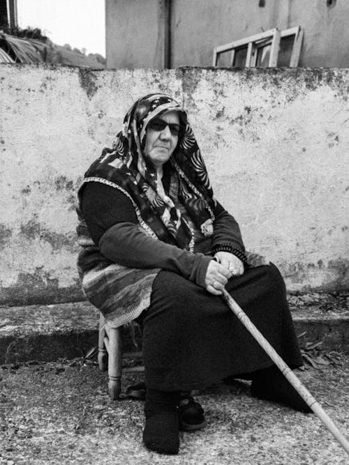 An old woman sitting on a chair with a cane