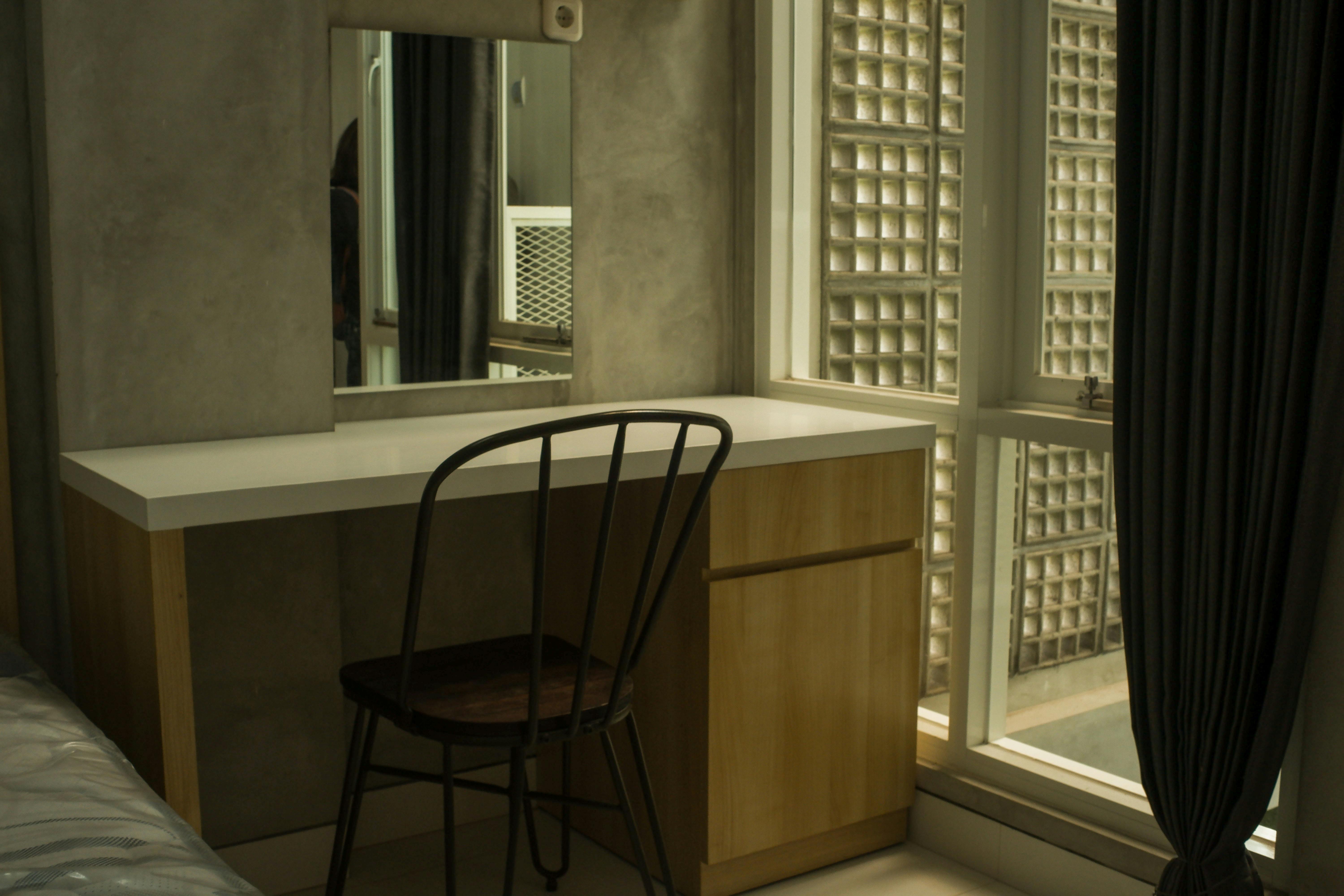 what is residential assisted living - A minimalist indoor space featuring a vanity table with a mirror and a metal chair by a window.