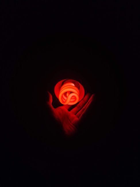 A red glowing compact fluorescent light bulb in a human hand against a dark background.