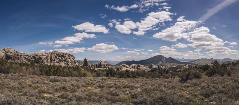 Panoramic view of majestic rocky formations with a clear blue sky and fluffy clouds.