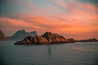 挪威特罗姆斯的岩石岛屿与山脉间，日落景色令人惊叹，温暖的光芒在海面上荡漾