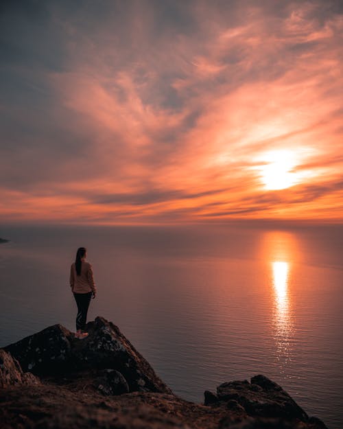 Woman Standing On Mountain Edge Looking At Sunset