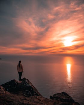 在挪威特罗姆斯的岩石悬崖上，人们欣赏着海洋上令人惊叹的日落