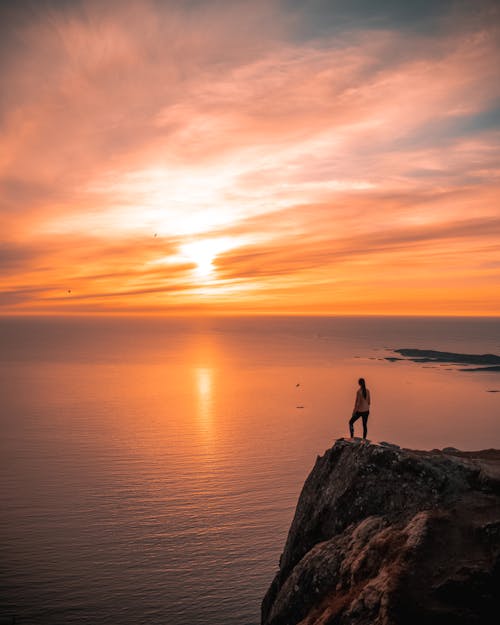 A Person Standing on a Cliff Overlooking the Sea during Golden Hour