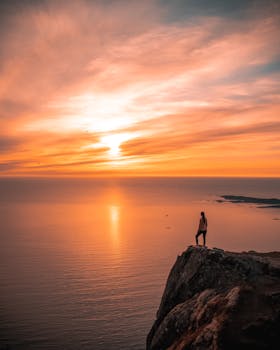 在挪威特罗姆斯的悬崖上，一个人正欣赏着海洋上令人惊叹的日落