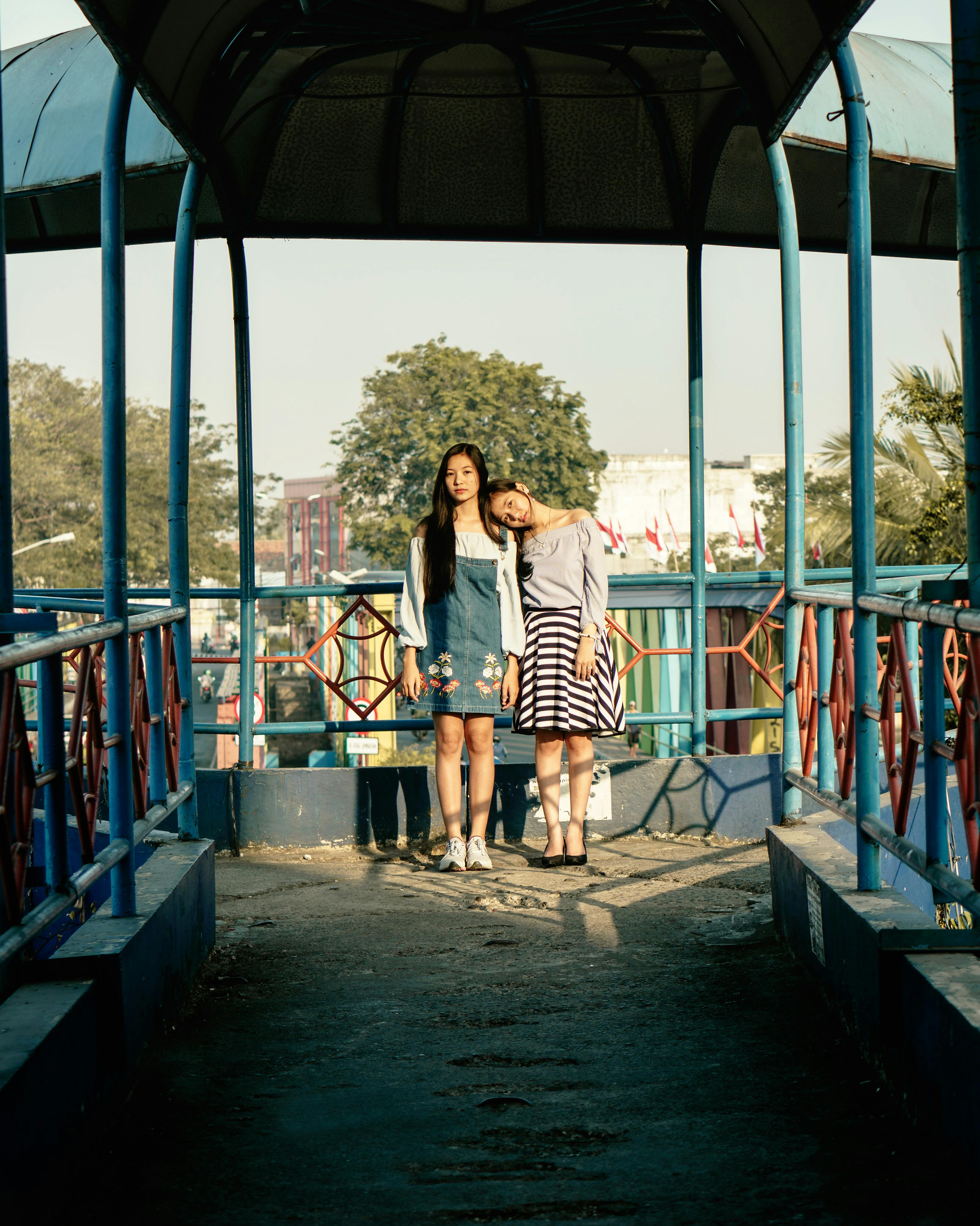 Two women standing on a colorful footbridge in daylight, expressing friendship and style.